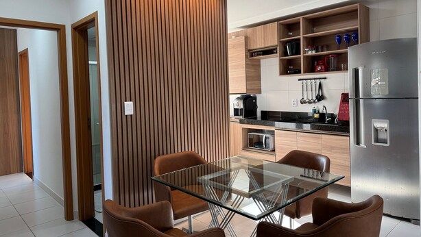 Une cuisine moderne avec une table à plateau en verre et des chaises marron, un réfrigérateur en acier inoxydable et des meubles de cuisine en bois.