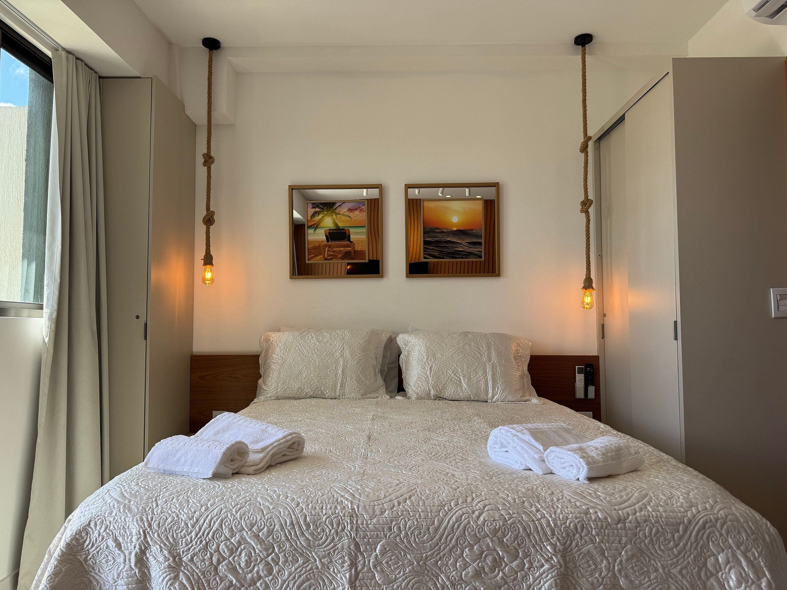 Quarto de hotel com uma cama grande, duas pinturas penduradas na parede e uma janela com cortinas.