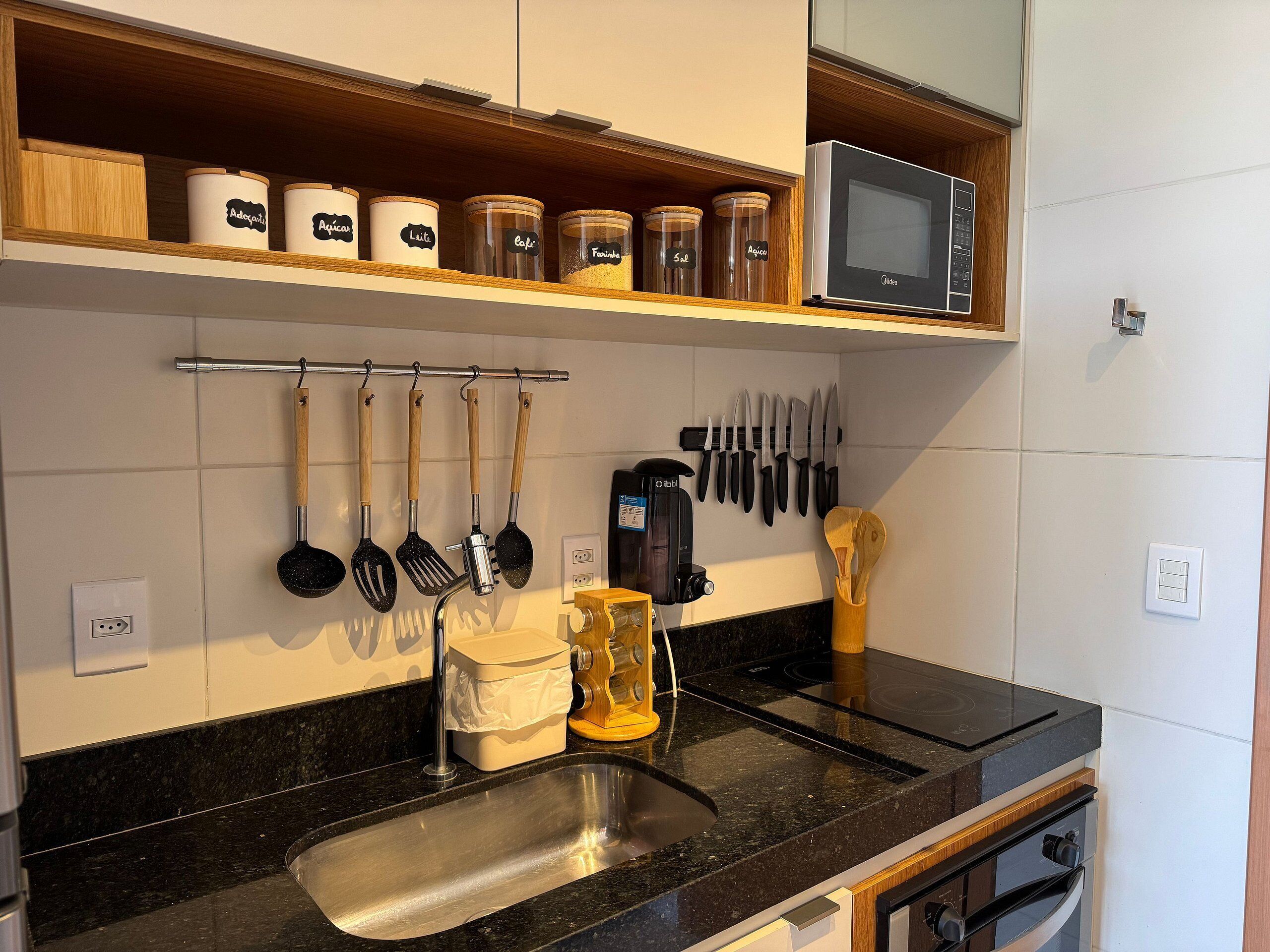 Una cocina con un lavamanos de acero inoxidable, una cafetera y diversos utensilios colgados en la pared.