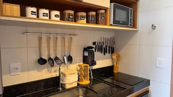 Una cocina con un lavamanos de acero inoxidable, una cafetera y diversos utensilios colgados en la pared.