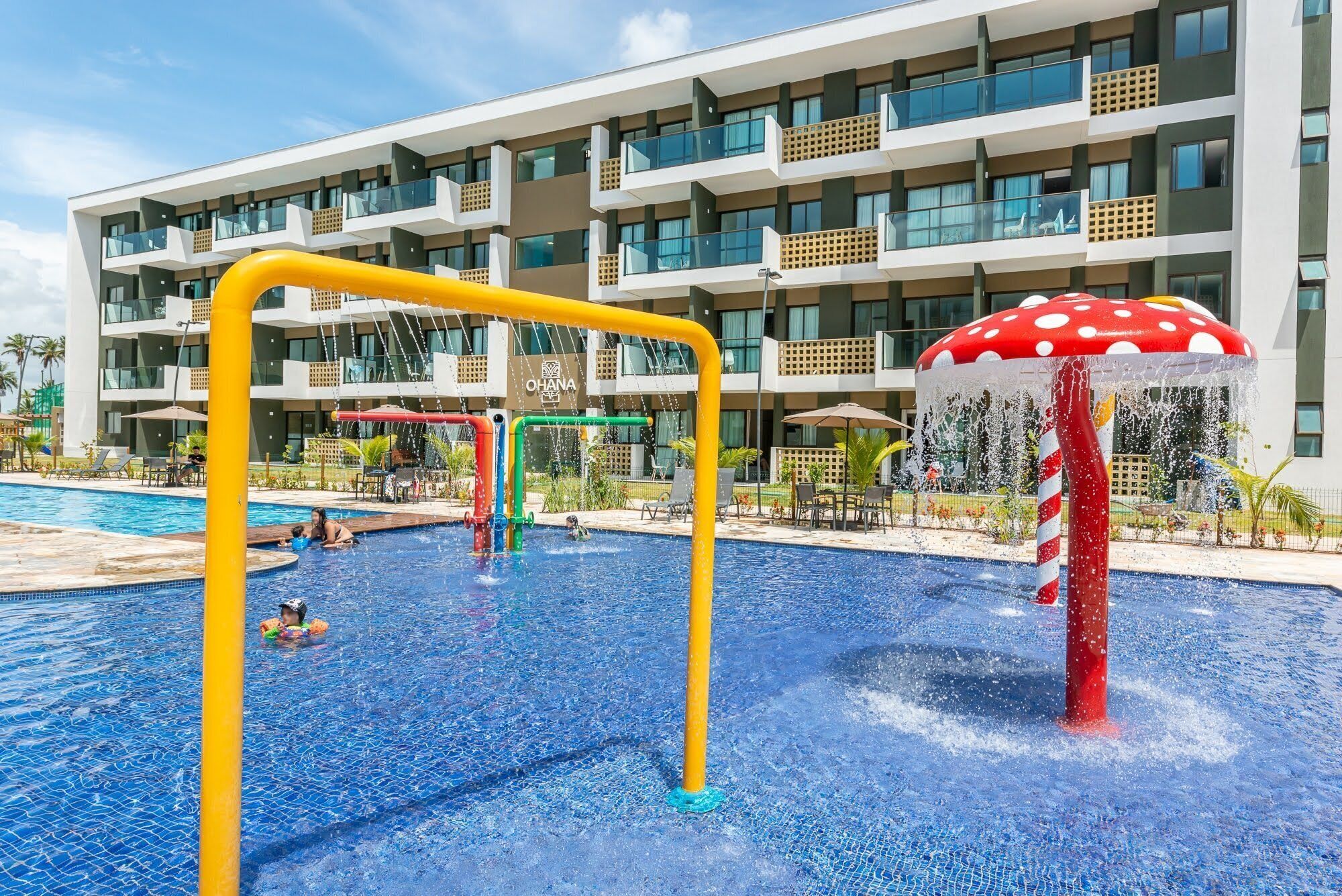 Ein Schwimmbad mit Wasserspielen und ein modernes Hotelgebäude im Hintergrund.