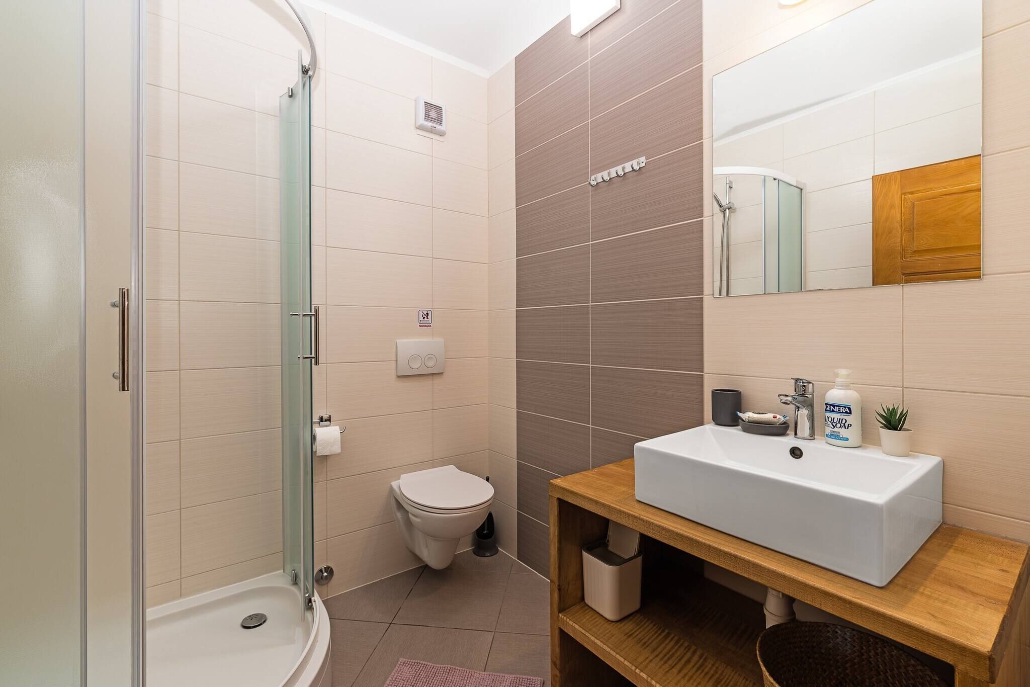 Un baño moderno con cabina de ducha de vidrio, inodoro, lavabo con espejo y una pequeña planta en maceta.