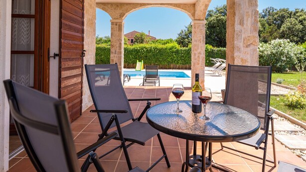 Un porche cubierto con una mesa redonda y dos sillas, con vistas a una piscina y follaje.