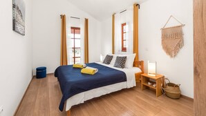 Un dormitorio ordenado con cama, mesita de noche, lámpara y un tapiz de macramé.