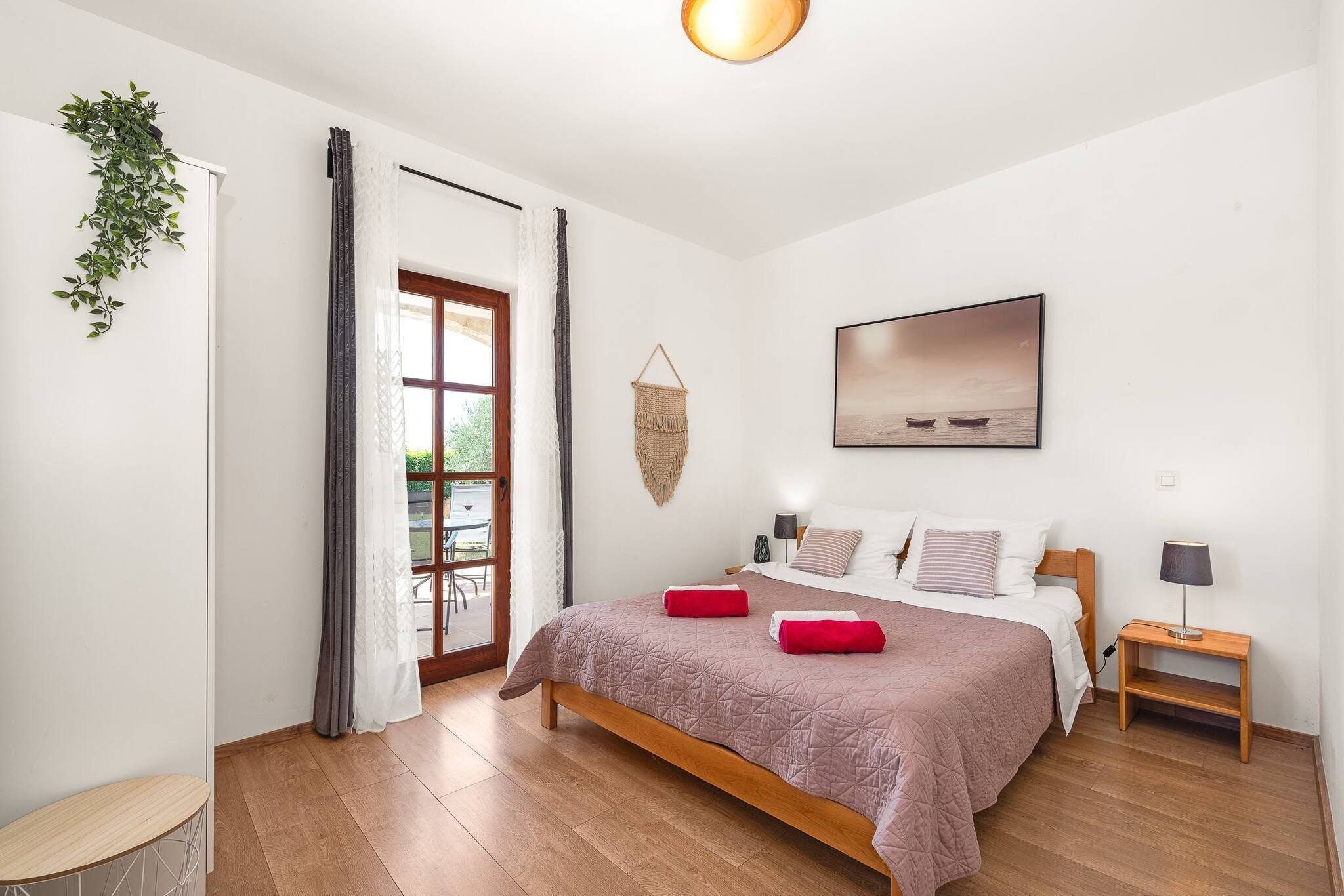 A bedroom with a bed, a bedside table, a hanging macrame wall decoration, and a window with curtains.