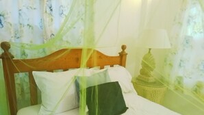 Un lit avec une tête de lit en bois, une literie blanche et un oreiller vert. Une lampe se trouve sur une table de chevet, et un objet décoratif est accroché au mur.