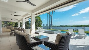 A spacious outdoor patio with wicker furniture, a glass table, and a view of a body of water and city skyline. - 5 Min Walk to Beach - Secluded Beachside Haven with Heated Pool, Water Toys, Privacy & (Bonita Springs)