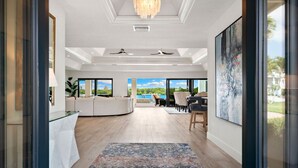 A spacious living area with a large window, a ceiling fan, and a modern chandelier. - 5 Min Walk to Beach - Secluded Beachside Haven with Heated Pool, Water Toys, Privacy & (Bonita Springs)