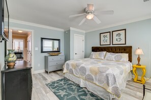 Un dormitorio con cama, ventilador de techo, cómoda, mesita de noche y cuadros en la pared.