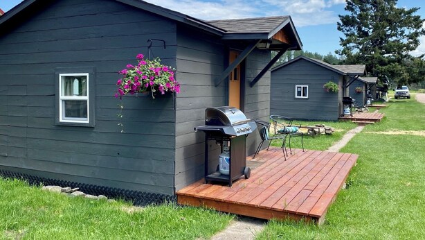A row of cabins with a barbecue grill, a hanging flower basket, and a clear sky.
