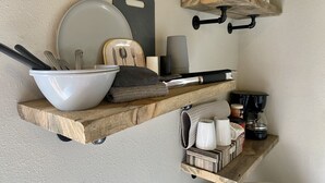 A kitchen shelf with a bowl, utensils, a cutting board, and a coffee maker.