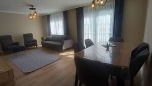 Ein geräumiger Wohnbereich mit Holzboden, einem runden Esstisch und mehreren Stühlen. In der Mitte befinden sich zwei Sofas und ein kleiner Teppich.