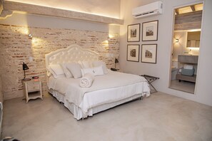 A bedroom with a brick wall, a large bed, a nightstand, a wall-mounted air conditioner, and framed pictures. - Lunala Hotel Boutique  (Cartagena)