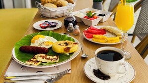 Een ontbijttafel met diverse soorten eten, waaronder eieren, worstjes en fruit, plus een kop koffie en een glas sinaasappelsap.