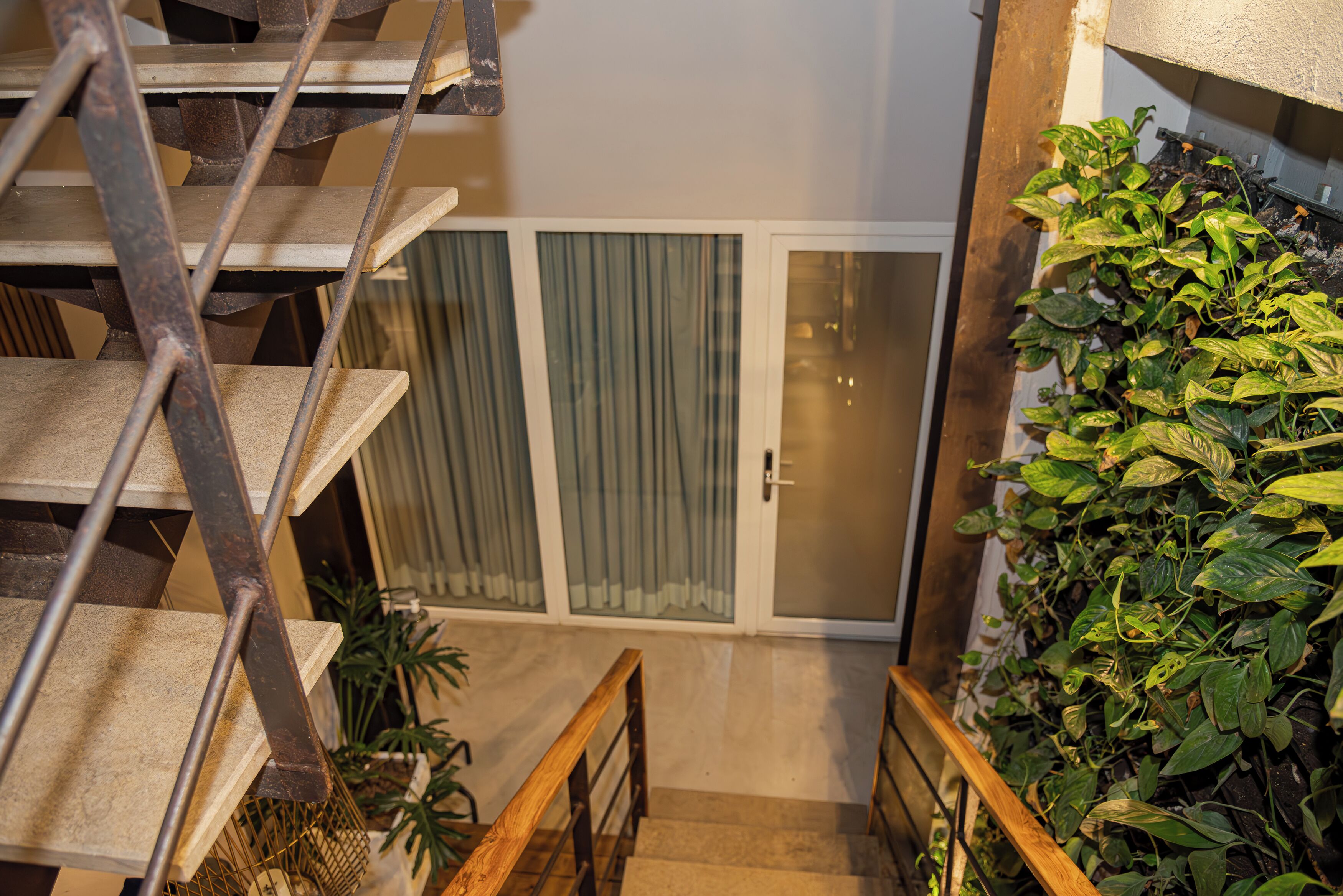 A staircase with metal railings leading to a room with a sliding glass door and a green plant wall.