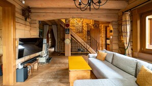 L’intérieur d’une cabane en rondins, avec une grande télévision, des meubles en bois, un escalier et un tapis jaune.