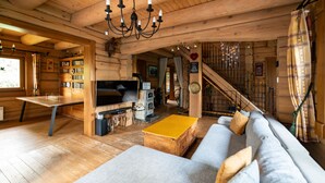 L’intérieur d’un chalet confortable, avec des murs en bois, un escalier en bois, un canapé, un téléviseur et une bibliothèque.