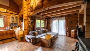 L’intérieur chaleureux d’un chalet en bois présente un grand canapé en forme de L, un plancher en bois et un coin cuisine avec des armoires en bois et un évier.