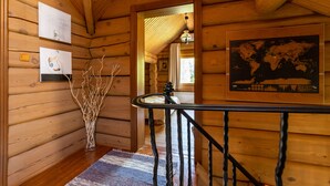 L’intérieur d’un chalet en bois, avec un escalier, des murs en bois, une carte du monde et un vase décoré de branches.
