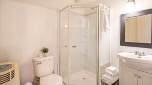 Baño con inodoro, ducha con mampara de vidrio, lavamanos y espejo.
