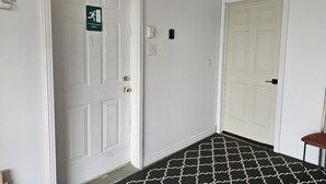Un pasillo con dos puertas blancas, una señalizada con la indicación de salida, y un tapete estampado en el suelo.