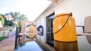 Un contenedor amarillo con una correa negra sobre una superficie reflectante, probablemente una mesa, con vista a un patio al fondo.