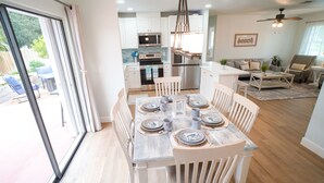 Un comedor con una mesa lista para seis comensales, una cocina al fondo y vistas al exterior a través de un ventanal corredero.