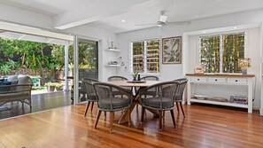 A modern dining area with a wooden table and wicker chairs, a white console table with decorative items, and a glass door leading to a garden.