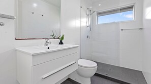 A modern bathroom with a white vanity, a toilet, a shower, and a window providing natural light.