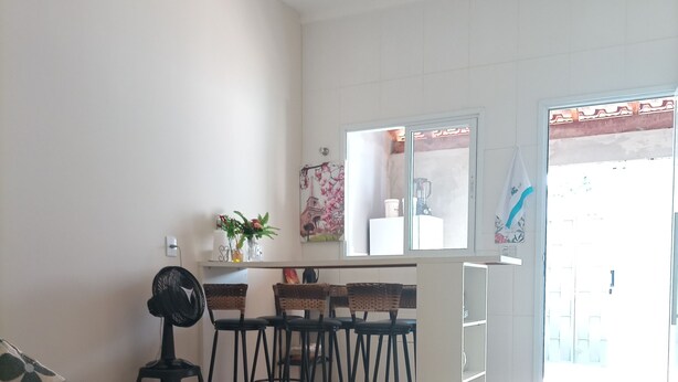 A living room with a sofa, a coffee table, and a patterned rug. There is a kitchen area with a counter, stools, and a refrigerator.