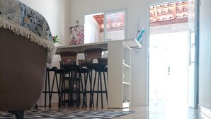 A modern kitchen with a dining area, featuring a large window, a patterned rug, and a tiled floor.