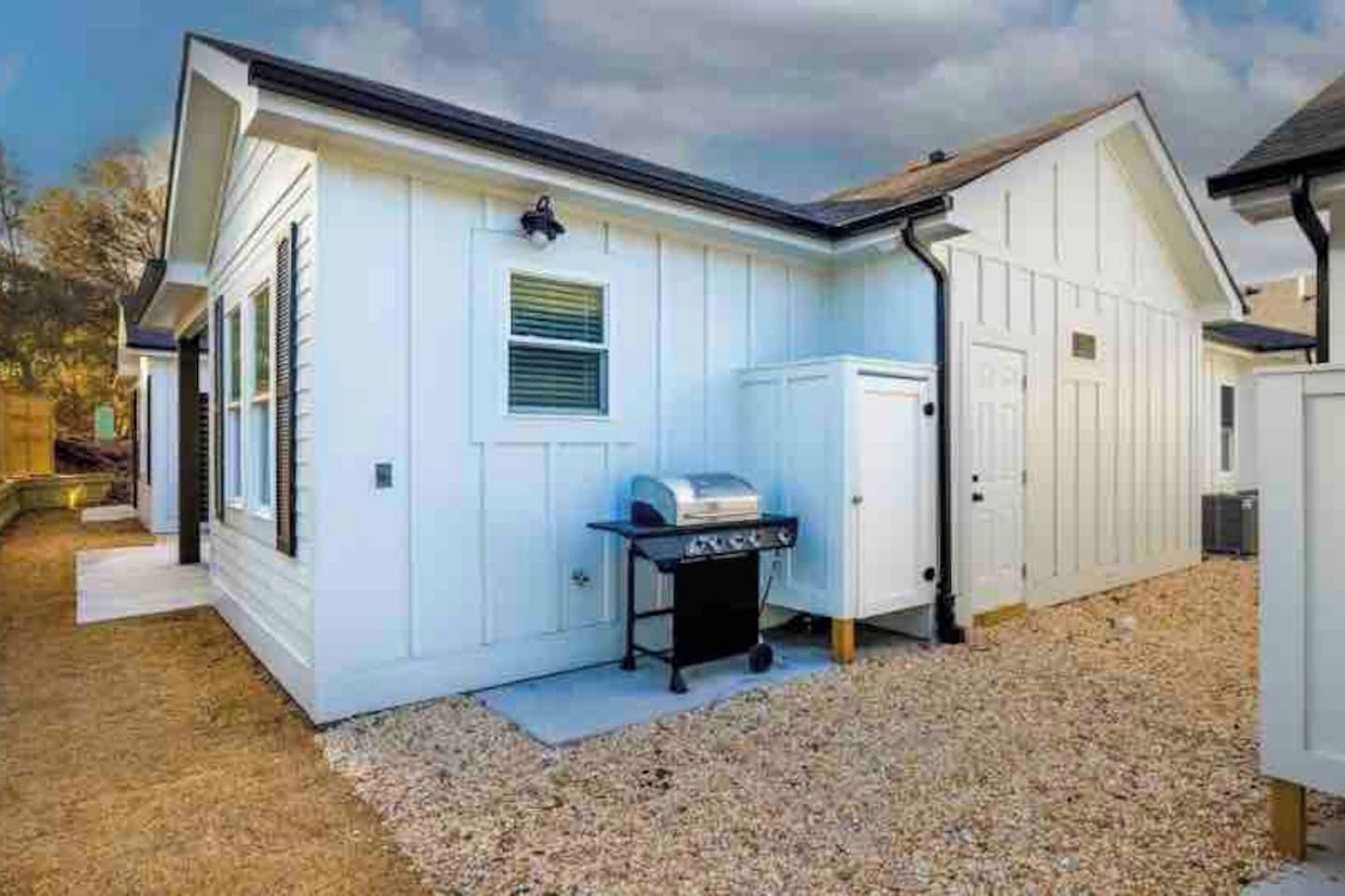 A white building with a garage door, a grill, and a shed.