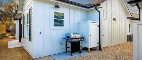A white building with a garage door, a grill, and a shed.