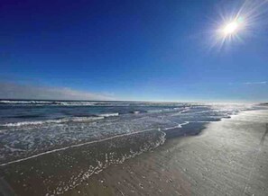 A beach with waves, a clear sky, and the sun shining.