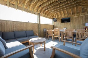 Relax on the patio with a sofa, table, and chairs under a rustic ceiling.