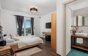 Quarto com cama, televisão, escrivaninha e banheiro com pia e espelho.