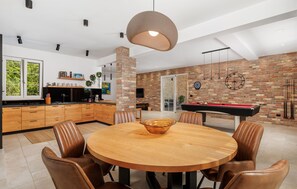 A modern kitchen with wooden cabinets, a dining area with a round table and leather chairs, a brick wall, and a pool table. - Beautiful home in Dobrinj (Dobrinj)