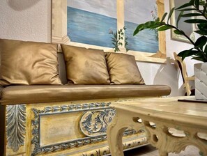 Relax in a stylish room with a sofa, chair, and small table, set against a seascape painting and ornate walls.