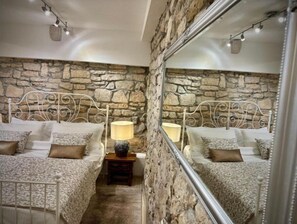 Two beds with matching metal headboards and bedding, a wooden nightstand, and a large mirror create a cozy atmosphere.