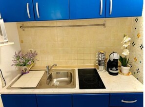 Compact kitchen with stainless steel sink, induction cooktop, and blue cabinets.