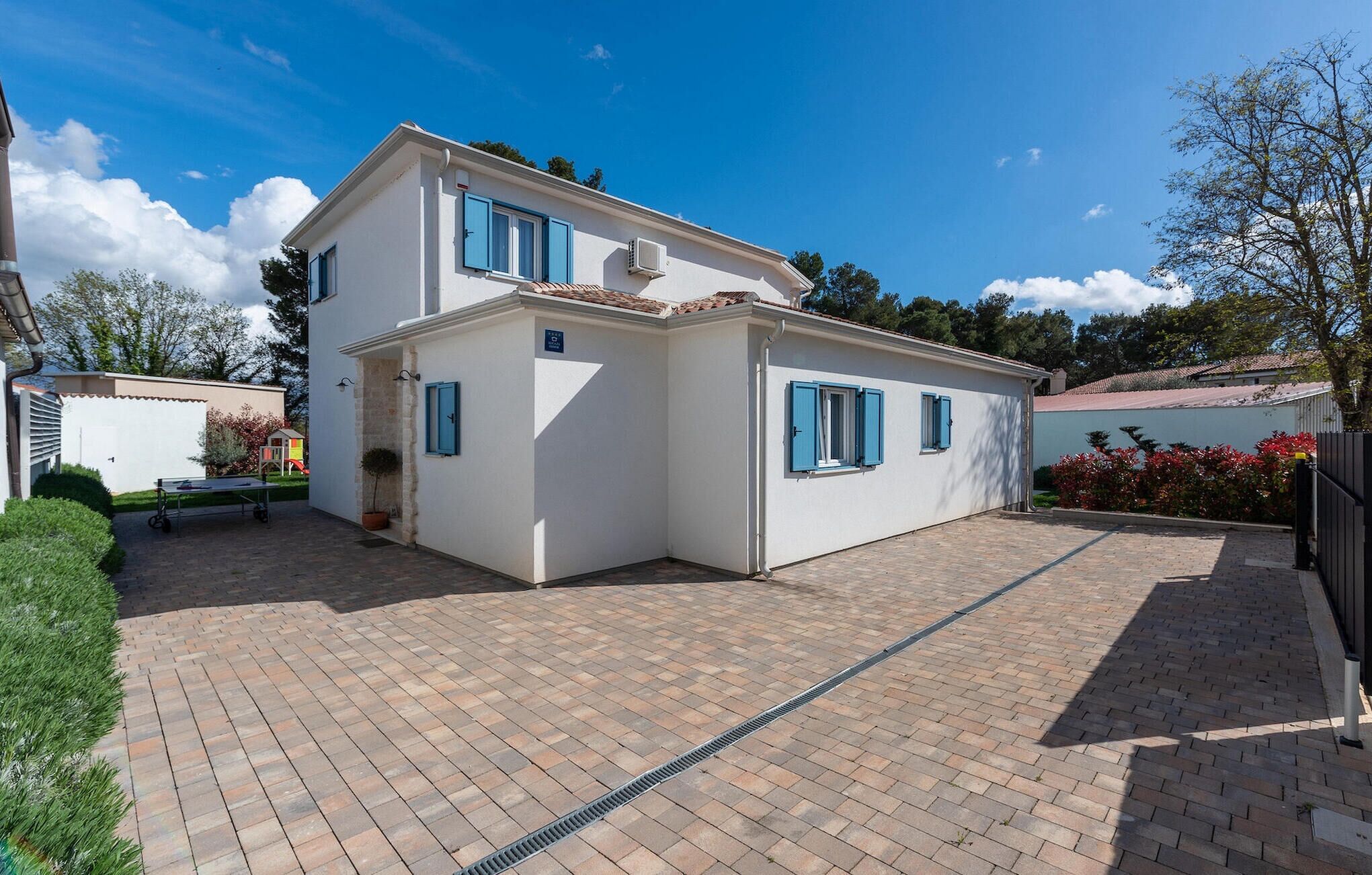 Une maison à deux étages avec une cour pavée, un petit jardin et un appareil de climatisation visible.