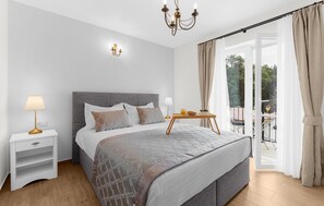 Een moderne slaapkamer met een groot bed, nachtkastjes, een kroonluchter en uitzicht op een balkon.