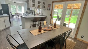 A modern kitchen with a central island, dark chairs, and a dining table with candles. - Private Mountain Retreat in the Woods! (Columbia Falls)