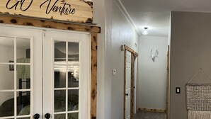 A hallway with a wooden sign reading "GO Adventure," a white door with glass panels, and a wall-mounted decorative animal head. - Private Mountain Retreat in the Woods! (Columbia Falls)