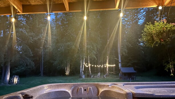 A hot tub area with a wooden deck, surrounded by trees and string lights. - Private Mountain Retreat in the Woods! (Columbia Falls)