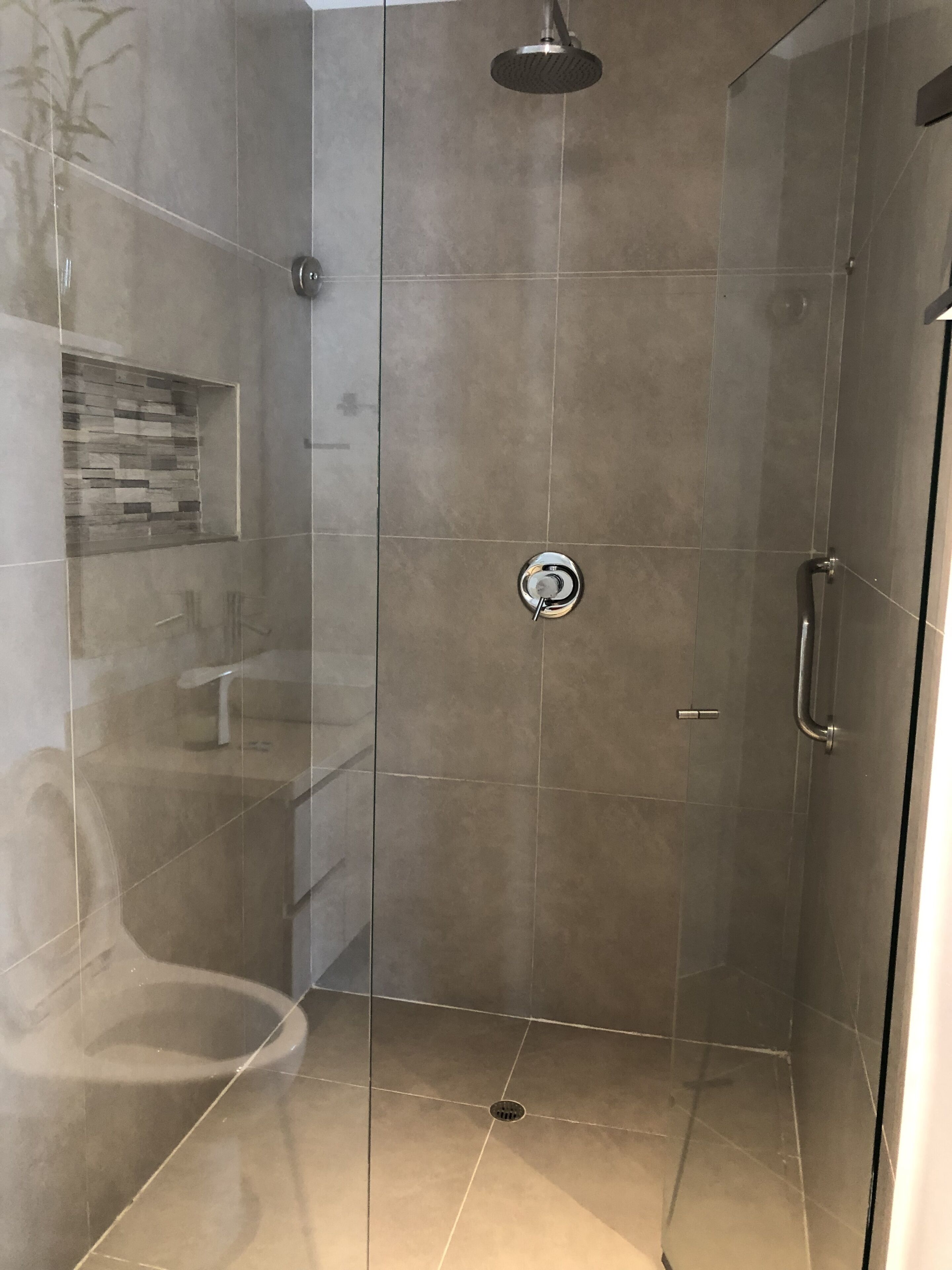 Una ducha moderna con puerta de vidrio, ducha de lluvia y barra de apoyo.