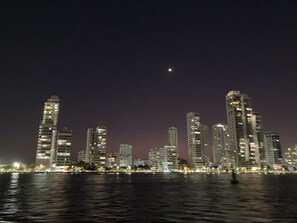 Une vue nocturne d’une ville avec de hauts immeubles le long d’une promenade au bord de l’eau.