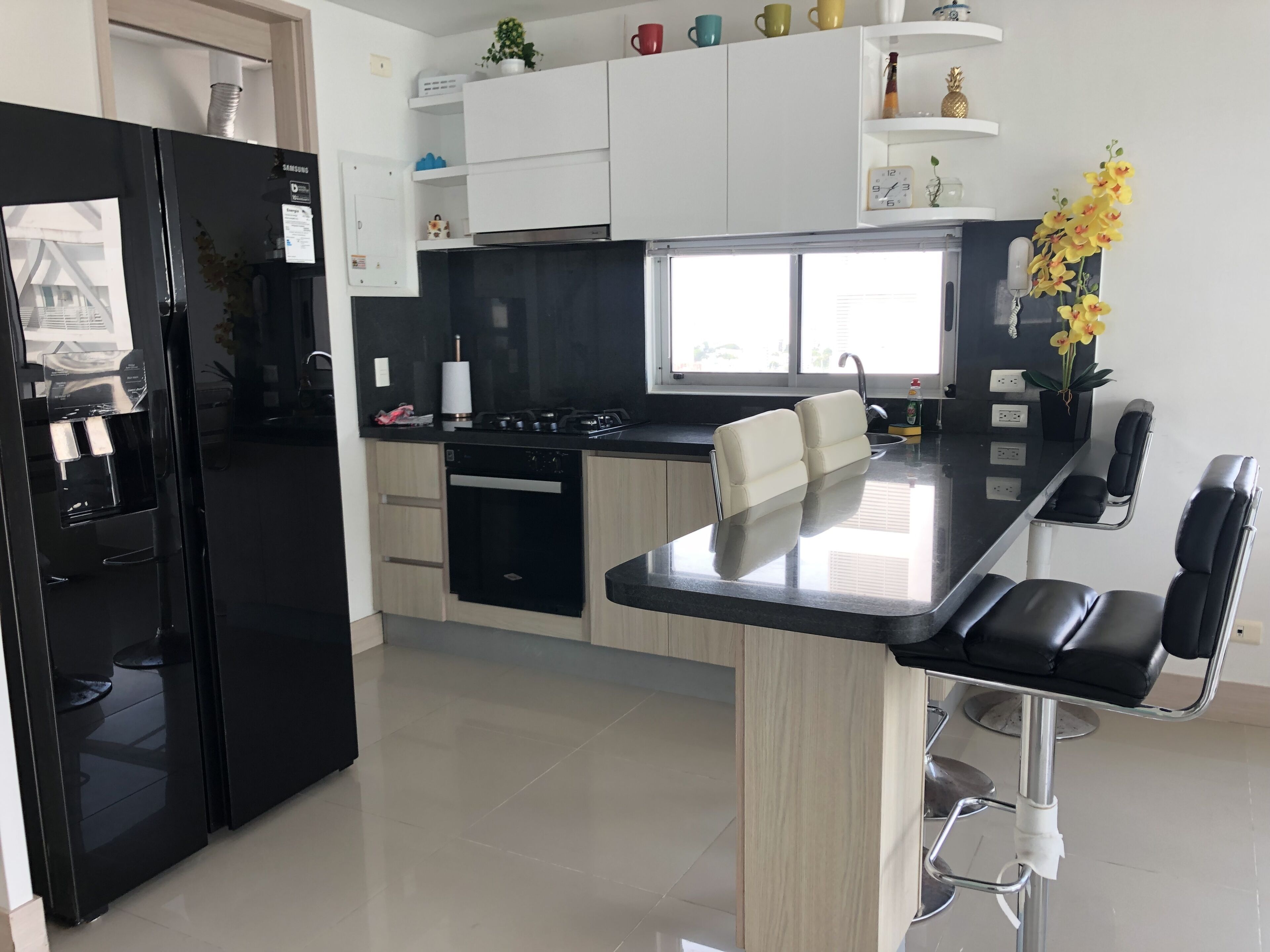 Una cocina moderna con un refrigerador negro, horno empotrado e isla de acero inoxidable con taburetes de bar.
