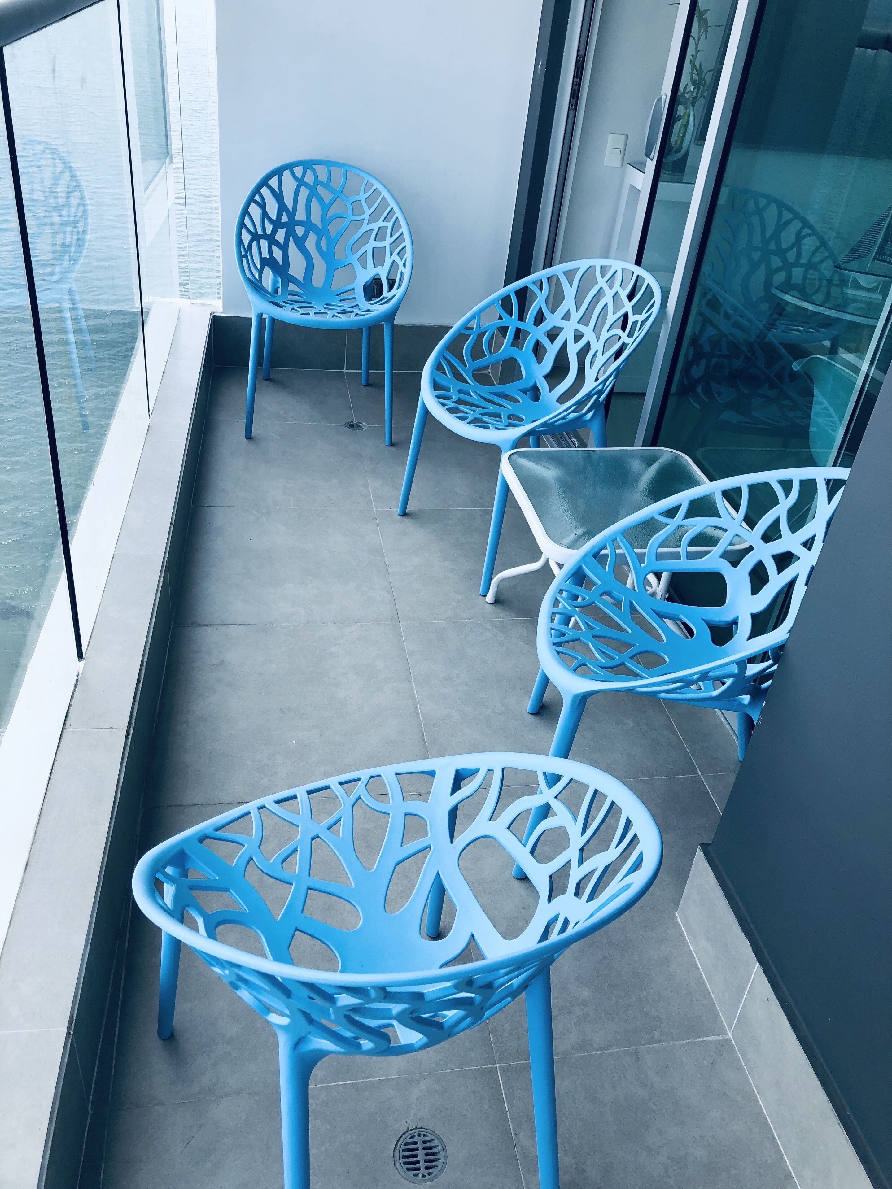 Een balkon met vier blauwe stoelen en een kleine tafel, een glazen hekwerk en uitzicht op het water.