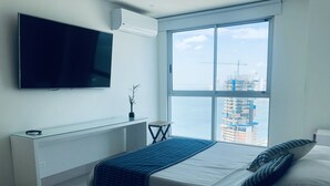 A modern hotel room with a large bed, a TV mounted on the wall, a window with a view of a cityscape, and a small table with a plant. - MURANO ELITE  GRADIMAR (Cartagena)